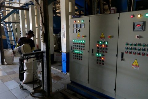 Pekerja menuangkan beras ke dalam karung di dekat panel kelistrikan yang menopang mesin penggilingan padi.