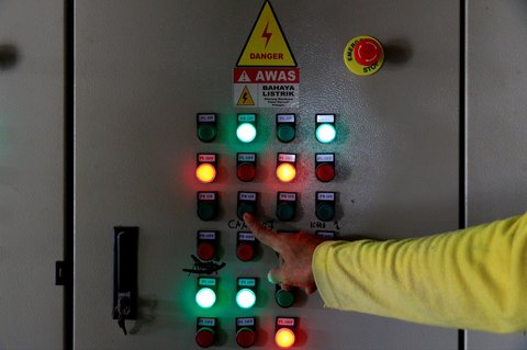 Pekerja mengoperasikan panel listrik yang menopang mesin penggilingan padi.