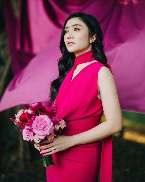 Febby tampil menawan dalam dress pink cerah karya Pamela Usanto, dipadukan dengan bunga senada dan latar belakang pink magenta yang mencolok.<br><br>