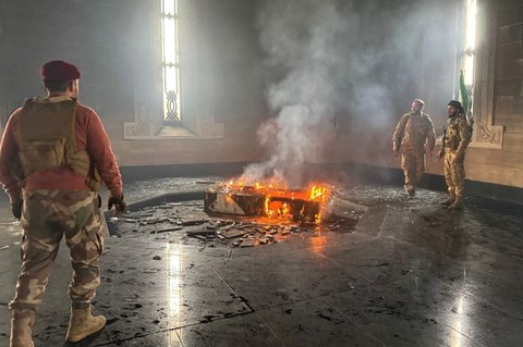 Pejuang pemberontak berdiri di makam ayah Bashar Al-Assad, Hafez al-Assad, yang terbakar di Qardaha, desa leluhur keluarga Assad, di barat laut Suriah, pada 11 Desember 2024.