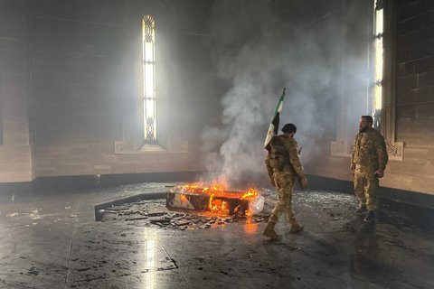 Pejuang pemberontak berdiri di makam ayah Bashar Al-Assad, Hafez al-Assad, yang terbakar di Qardaha, desa leluhur keluarga Assad, di barat laut Suriah, pada 11 Desember 2024.