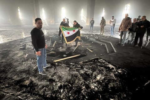 Pejuang pemberontak berdiri di makam ayah Bashar Al-Assad, Hafez al-Assad, yang hangus tak bersisa setelah dibakar di Qardaha, desa leluhur keluarga Assad, di barat laut Suriah, pada 11 Desember 2024.
