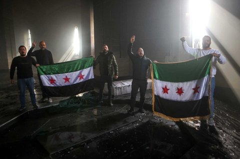 Pejuang pemberontak berdiri di makam ayah Bashar Al-Assad, Hafez al-Assad, yang hangus tak bersisa setelah dibakar di Qardaha, desa leluhur keluarga Assad, di barat laut Suriah, pada 11 Desember 2024.