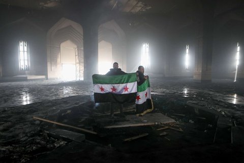 Pejuang pemberontak berdiri di makam ayah Bashar Al-Assad, Hafez al-Assad, yang hangus tak bersisa setelah dibakar di Qardaha, desa leluhur keluarga Assad, di barat laut Suriah, pada 11 Desember 2024.