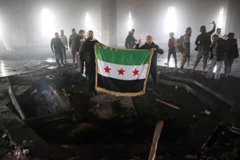 Pejuang pemberontak berdiri di makam ayah Bashar Al-Assad, Hafez al-Assad, yang hangus tak bersisa setelah dibakar di Qardaha, desa leluhur keluarga Assad, di barat laut Suriah, pada 11 Desember 2024.