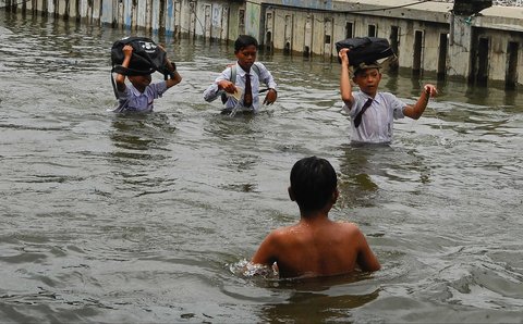 Sejumlah anak melewati genangan banjir rob saat sepulang sekolah di kawasan Muara Angke, Jakarta, Senin (16/12/2024).
