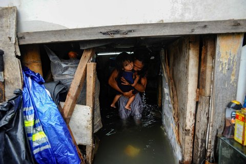 Seorang warga menggendong anaknya saat rumahnya terendam banjir rob yang melanda kawasan Muara Angke, Jakarta, Senin (16/12/2024).