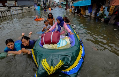 Sejumlah warga menggunakan perahu karet saat melewati banjir rob yang melanda kawasan Muara Angke, Jakarta, Senin (16/12/2024).