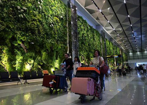 Penumpang pesawat  berjalan melewati lorong yang rimbun dengan suasana tanaman tropis di Terminal 3 Bandara Internasional Soekarno Hatta, Tangerang, Banten, Selasa (17/12/2024).