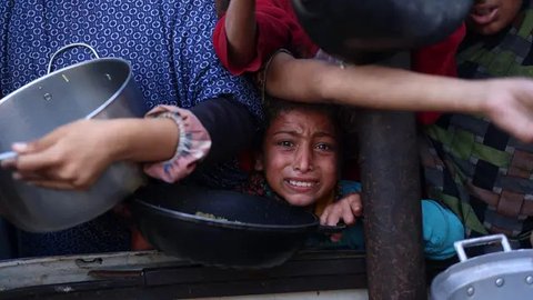 Seorang anak perempuan Palestina menunggu dalam antrean untuk menerima makanan di luar pusat distribusi di selatan Khan Yunis pada 6 Desember 2024. (BASHAR TALEB/AFP)