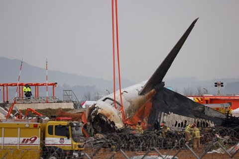 Petugas pemadam kebakaran berdiri di dekat reruntuhan pesawat Jeju Air yang menabrak pembatas dan meledak setelah tergelincir landasan pacu di Bandara Internasional Muan, Muan, Korea Selatan, pada 30 Desember 2024.