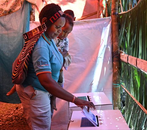 Seorang wanita menggendong anaknya saat mengikuti pemungutan suara Pemilu 2024 di Distrik Kwamki Narama, Mimika, Papua, Rabu (14/2/2024). Pemilu 2024 berlangsung di seluruh wilayah Indonesia, termasuk Papua. Adek Berry/AFP