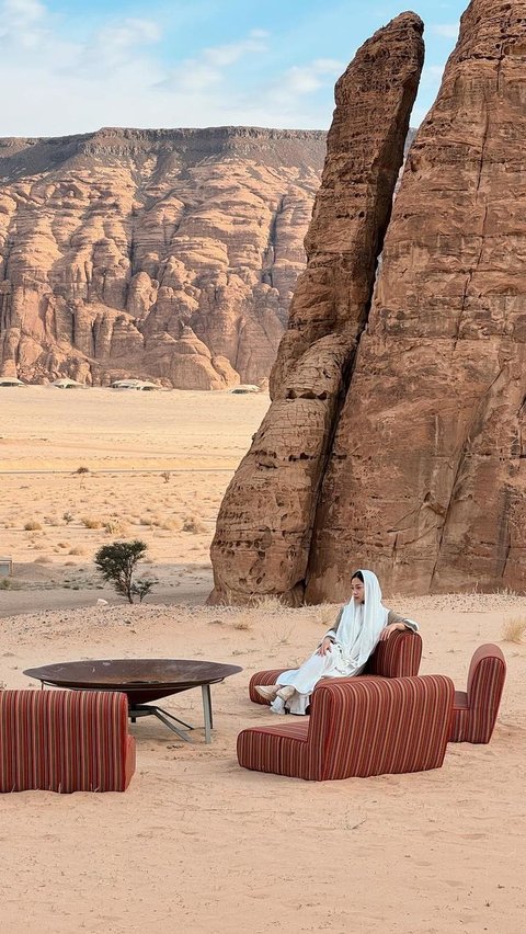 Di tengah padang pasir yang dikelilingi oleh pegunungan batu yang menjulang, Nikita terlihat santai duduk di atas sofa.