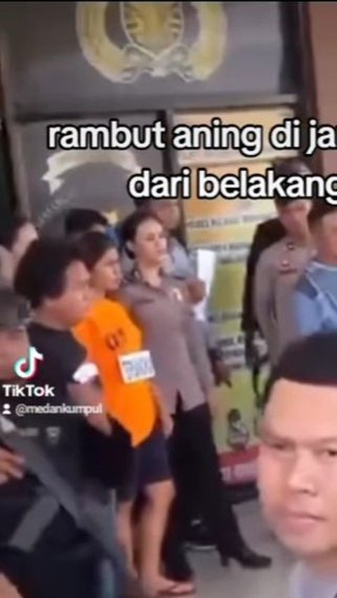 Mengenakan baju orange, Aning terlihat didampingi oleh polisi saat berdiri di depan kantor polisi.