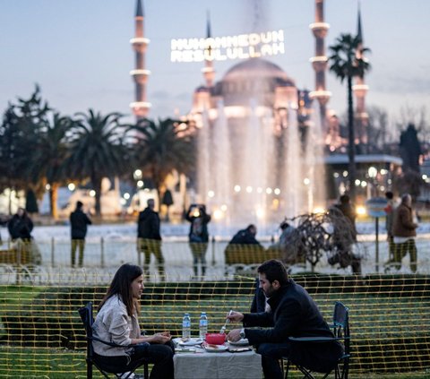 Sepasang suami istri berbagi makanan berbuka dengan latar belakang Masjid Biru di Alun-Alun Sultan Ahmed, Istanbul, Turki, pada hari pertama Ramadan, Senin (11/3/2024). Kota Istanbul di Turki menawarkan suasana Ramadan yang sangat unik. Yasin Akgul/AFP
