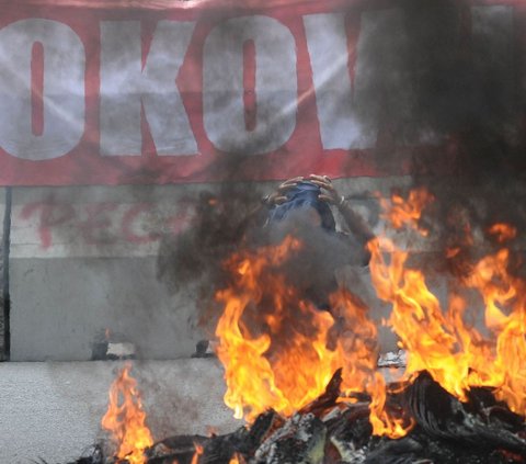 Pendemo melakukan aksi membakar ban saat protes di depan Kantor Komisi Pemilihan Umum (KPU), Jakarta, Senin (18/3/2024). Aksi demonstrasi ini dilakukan oleh sebagian besar pendukung pasangan calon presiden dan wakil presiden 01 dan 03. Foto: merdeka.com / imam buhori