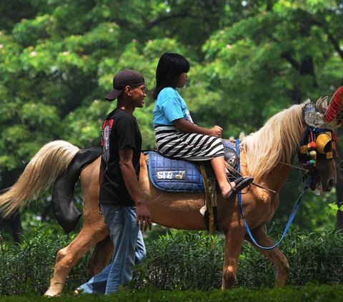 Seorang anak tampak antusias menunggang kuda saat menikmati jalan-jalan di Kawasan Kanal Banjir Timur, Jakarta Timur, Kamis (11/4/2024). Mengisi waktu libur Lebaran sejumlah warga mulai mencari lokasi wisata. Foto: merdeka.com / Imam Buhori<br>
