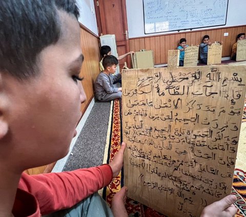 Di sebuah masjid di Tripoli, Libya, sejumlah anak masih belajar membaca dan menulis ayat-ayat Alquran menggunakan cara yang unik, yaitu papan kayu selama bulan suci Ramadhan pada tanggal 3 April 2023. Foto: REUTERS / Ayman al-Sahili<br>