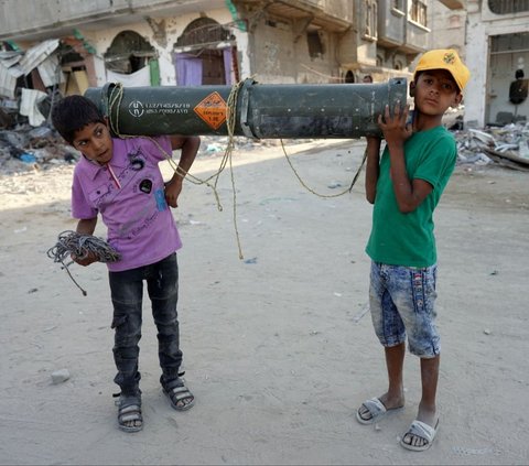 Dua orang anak mengangkat sisa amunisi Amerika Serikat di Khan Younis, Jalur Gaza selatan, pada Kamis (16/5/2024). Sisa-sisa amunisi yang telah kosong tersebut menjadi salah satu jejak serangan brutal Israel ke Jalur Gaza. Foto: AFP