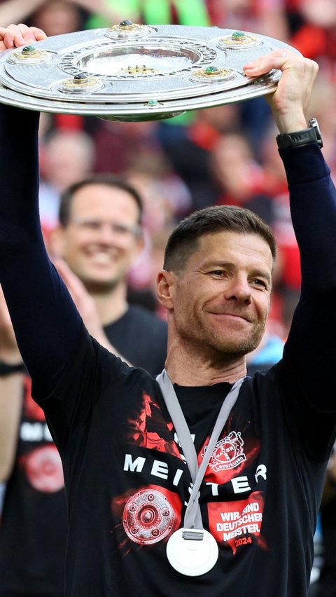 Senyum Xabi Alonso mengangkat trofi juara Bundesliga 2023/2024 yang diraih Bayer Leverkusen. Foto: REUTERS/Wolfgang Rattay