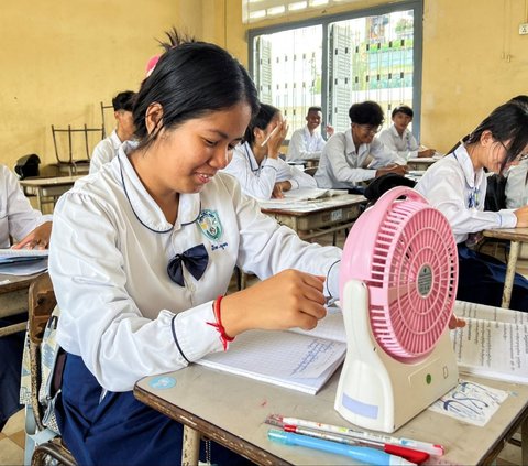 Seorang murid menggunakan kipas angin untuk menyegarkan diri selama kebiatan belajar di sebuah sekolah di Phnom Penh, Kamboja, pada Kamis (2/5/2024). Gelombang panas yang membuat suhu naik ekstrem tengah 'memanggang' Kamboja. REUTERS/Cha Tha Lach