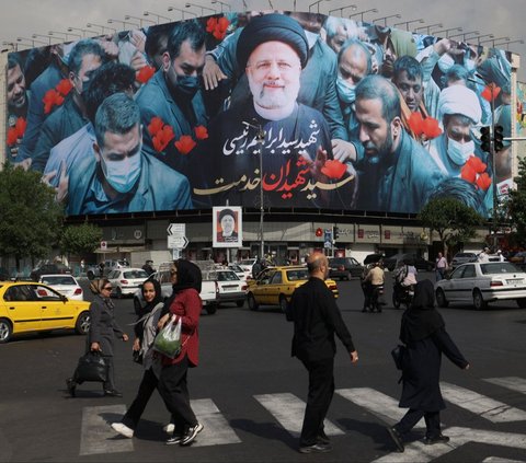 Sejumlah orang berjalan di depan baliho yang menampilkan almarhum Presiden Iran Ebrahim Raisi di Ibu Kota Teheran, Iran, Selasa (21/5/2024). Iran menetapkan masa berkabung selama lima hari untuk mengenang Presiden Ebrahim Raisi. Foto: Majid Asgaripour/WANA via REUTERS