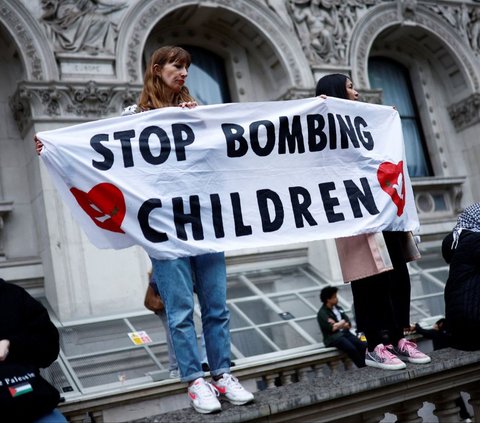 Pengunjuk rasa membentangkan spanduk bertuliskan 'Stop bombing children' saat menggelar aksi solidaritas untuk Palestina di London, Inggris, pada 28 Mei 2024. Dalam aksinya, ribuan pengunjuk rasa di London ini mengecam genosida yang dilakukan Israel di Jalur Gaza, Palestina. Foto: Benjamin Cremel/AFP