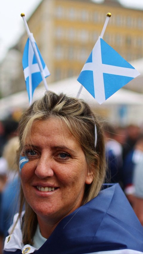 Seorang wanita tampil dengan atribut bendera Skotlandia di kepala dan wajahnya. Foto: REUTERS/Leonhard Simon