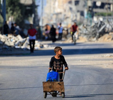 Seorang anak laki-laki membawa air di kamp pengungsi Al-Bureij, Jalur Gaza, Palestina, pada 24 Juni 2024. Blokade ketat dan serangan tanpa henti yang dilancarkan Israel sejak konflik terbaru meletus pada 7 Oktober 2023 menyebabkan Jalur Gaza dilanda krisis air bersih. Foto: Eyad Baba/AFP