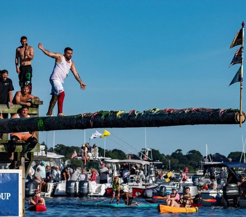 Peserta berjalan di tiang yang licin saat berkompetisi dalam Kontes Tiang Berminyak ke-94 dalam Perayaan Santo Petrus di Pantai Pavillion di Gloucester, Massachusetts, pada tanggal 28 Juni 2024. Foto: JOSEPH PREZIOSO / AFP<br>