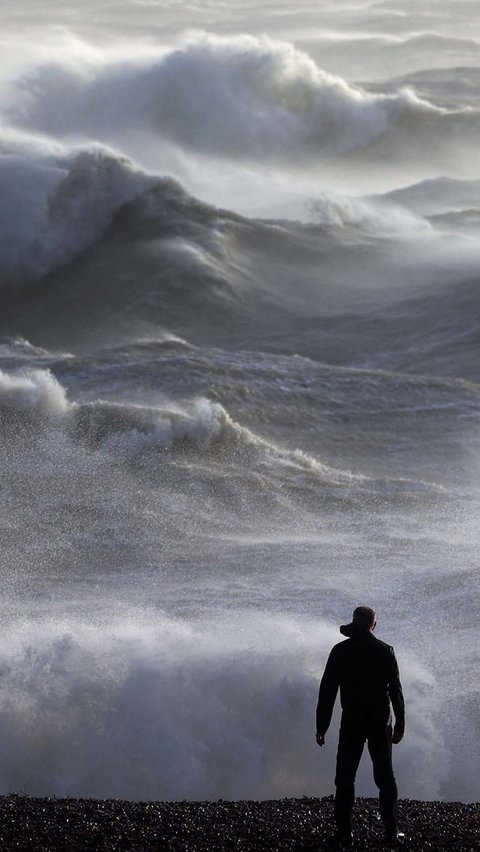 Seseorang melihat ke arah ombak yang menerjang pantai di Newhaven pada tanggal 2 Januari 2024. (ADRIAN DENNIS/AFP)