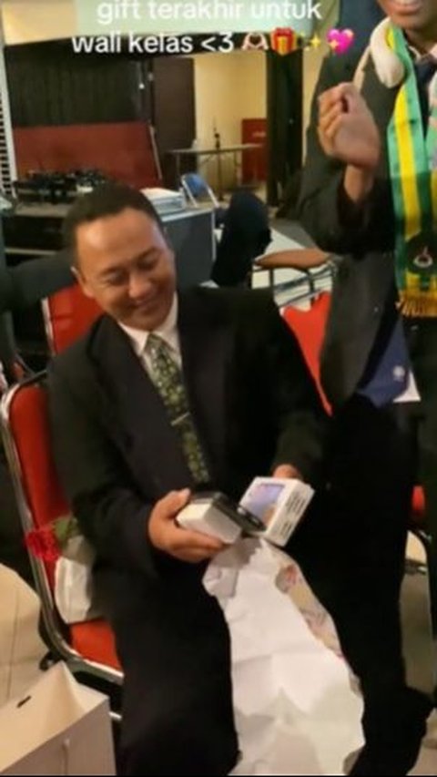 Saat dibuka, ia tampak terkejut dan tersenyum melihat hadiah berupa sebuah HP pemberian muridnya.