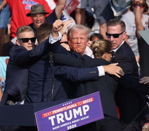 Mantan presiden Amerika Serikat yang juga kandidat presiden dari Partai Republik, Donald Trump mengangkat kepalan tangannya seraya mendapatkan perlindungan dari body guard setelah ditembak saat kampanye di Butler Farm Show, Butler, Pennsylvania, Amerika Serikat, pada Minggu (13/7) pagi WIB. Donald Trump tampak berlumuran darah di wajah dan telinganya setelah ditembak sniper dari jarak ratusan meter. Foto: REUTERS