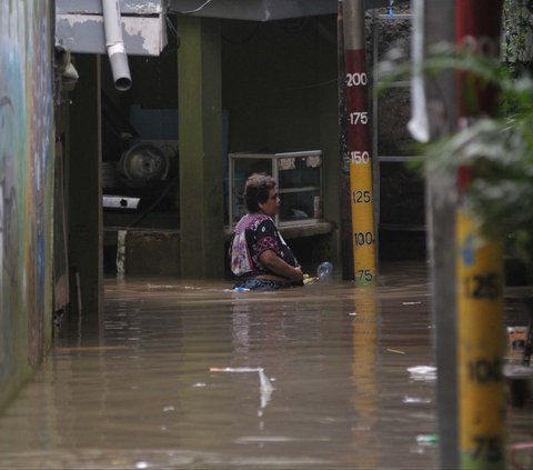 Seorang warga berjalan melewati banjir merendam permukiman di Kebon Pala, Jatinegara, Jakarta, Selasa (2/7/2024). Banjir ini terjadi akibat luapan Kali Ciliwung seiring tingginya intensitas hujan di wilayah Depok dan Bogor, Jawa Barat. Merdeka.com/Imam Buhori