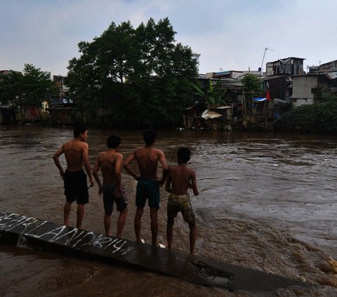 Sejumlah anak bersiap melompat pada aliran Kali Ciliwung yang mengalir deras di kawasan Bukit Duri-Manggarai, Jakarta, Selasa (2/7/2024). Derasnya arus sungai serta tingginya debit air tak menghalangi anak-anak untuk tetap bermain di Kali Ciliwung. Merdeka.com/Imam Buhori