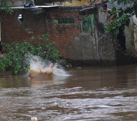 FOTO: Berbahaya! Aksi Nekat Anak-Anak Bermain di Tengah Derasnya Arus Kali Ciliwung