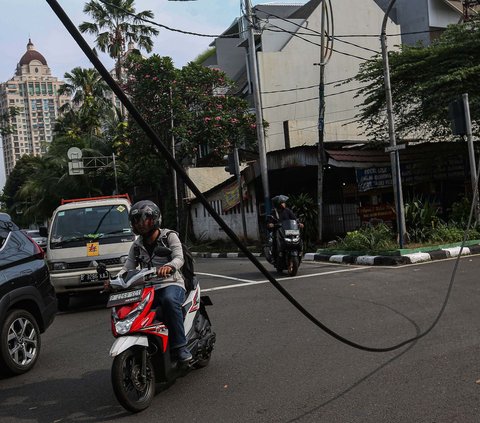 Sejumlah kendaraan melintas di dekat kabel menjuntai di Jalan Patal Senayan, Jakarta Selatan, Selasa (2/7/2024). Kabel tersebut menjuntai hingga nyaris menyentuh aspal setelah tersangkut pada sebuah truk bermuatan melebihi tinggi maksimum. Liputan6.com/Angga Yuniar