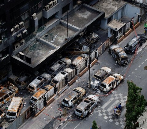 Seorang pria mengendarai becak melewati kendaraan rusak yang dibakar massa dalam aksi unjuk rasa di Dhaka, Bangladesh, pada 21 Juli 2024. Bangladesh dilanda kerusuhan berdarah selama berhari-hari ketika ribuan mahasiswa memprotes aturan baru terkait kuota penerimaan pekerja pemerintah atau PNS. Foto: REUTERS<br>