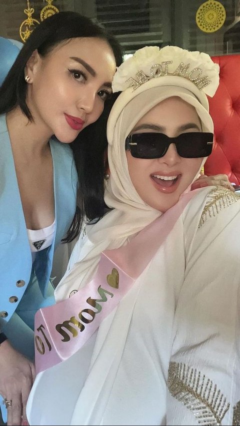 Syahrini mengenakan long dress putih dengan bando dan selempang pink bertuliskan 