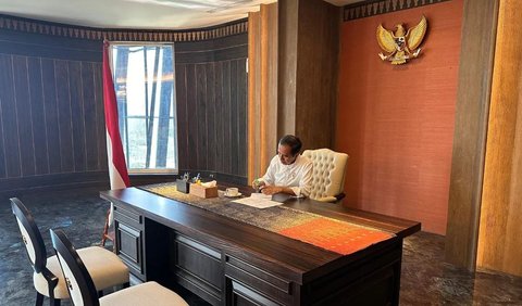 Pada foto pertama, Jokowi tampak duduk di belakang meja yang cukup besar di ruang kerja. Dia terliat memeriksa sejumlah dokumen di atas mejanya sambil memegang pulpen. Secangkir minuman tampak menemaninya.