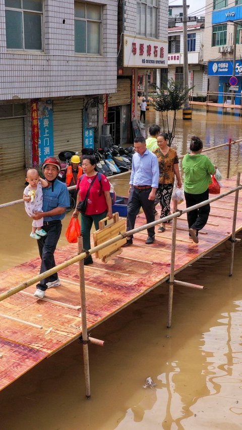 Warga yang melintasi jembatan darurat ini pun mengungkapkan rasa lega, aktivitas sehari-hari warga kota Maying dapat kembali berjalan lebih lancar, meskipun banjir masih menggenangi wilayah tersebut. Foto: STR / AFP<br>