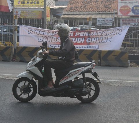 Pengendara melintas di dekat spanduk 'Tangkap dan Penjarakan Bandar Judi Online' yang terpampang di kawasan Mampang, Jakarta, Kamis (1/8/2024). Spanduk tersebut menyuarakan keresahan masyarakat terhadap menjamurnya praktik judi online. Foto: Merdeka.com/Imam Buhori<br>