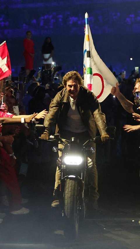 Tom Cruise juga bahkan menunggangi motor, mirip dengan adegan dalam film yang pernah dibintanginya, sambil membawa bendera Olimpiade. Foto: Reuters