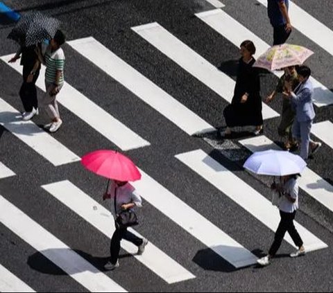 Pejalan kaki menggunakan payung saat menyeberangi jalan di Seoul, Korea Selatan, Rabu (14/8/2024). Gelombang panas ekstrem tengah melanda sebagian besar wilayah Korea Selatan. Foto: Anthony Wallace/AFP