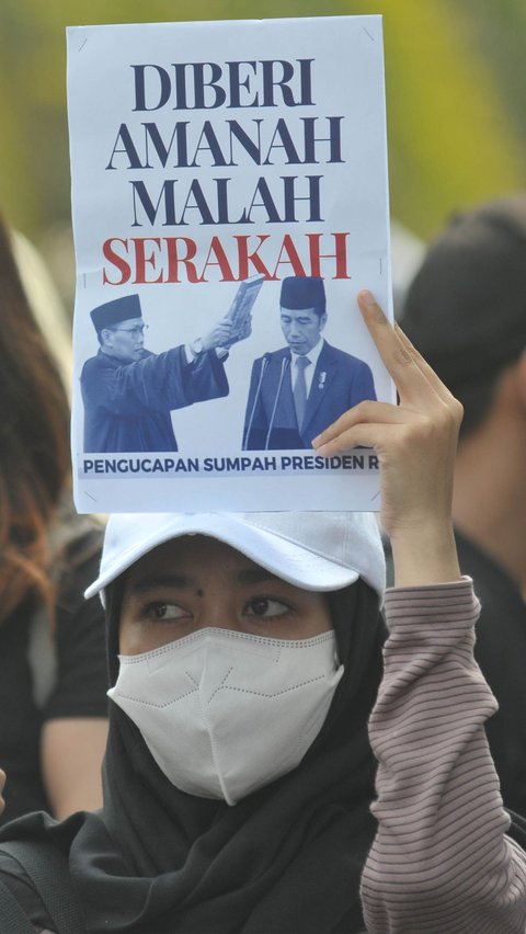 Pengunjuk rasa mengangkat poster bergambar Presiden Joko Widodo dengan tulisan: 