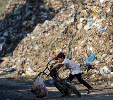 Seorang anak mendirikan sepedanya saat bermain di dekat sampah yang menggunung di kamp pengungsian Al-Maghazi di Jalur Gaza, Palestina, pada 2 Agustus 2024. Serangan brutal yang terus dilancarkan Israel membuat kehidupan warga Palestina di Jalur Gaza semakin terdesak. Foto: Eyad Baba/AFP