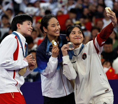 Pebulutangkis tunggal putri Indonesia, Gregoria Mariska tersenyum sembari memamerkan medali perunggu Olimpiade Paris 2024 saat berfoto bersama An Se Young asal Korea Selatan dan He Bing Jo asal China di Porte de La Chapelle Arena, Paris, Prancis, Senin (5/8/2024). Jorji, sapaan akrab Gregoria Mariska, berhasil meraih medali perunggu Olimpiade Paris 2024 dari nomor bulutangkis tunggal putri. Foto: Luis Tato/AFP