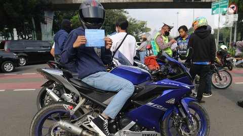 Seorang pengendara sepeda motor memperlihatkan surat tilang saat dilakukan razia knalpot bising di Monas, Jakarta, pada Minggu (7/3/2021). Direktorat Lalu Lintas Polda Metro Jaya telah menerapkan kebijakan yang melarang kendaraan bermotor dengan knalpot bising untuk melintas di area Monas pada hari Sabtu dan Minggu. (Liputan6.com/Herman Zakharia)