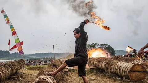 Seorang peserta menyalakan meriam yang terbuat dari batang pohon dengan menggunakan karbit dan air untuk menciptakan suara ledakan selama Festival Kuluwung, di Sukasirna, Jawa Barat, pada tanggal 5 April 2025. (ADITYA AJI/AFP)
