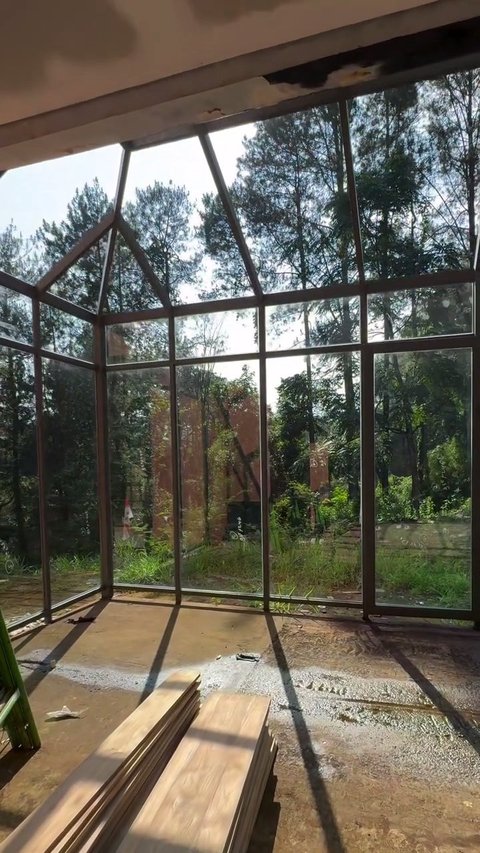 Ruang dengan dinding kaca besar, menyerupai green house, memperlihatkan view luar yang sangat hijau. Pencahayaan alami memenuhi ruangan ini.